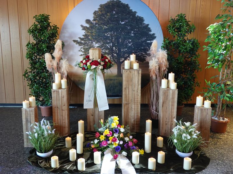Dekoration mit Kerzen, Blumen und Holzstelen vor einem Baumbild