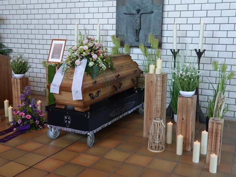 Holzsarg mit Gesteck und Kerzen vor weißer Klinkerwand