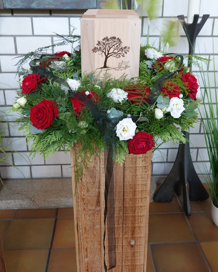 Urne mit Baumsymbol auf einer Holzstele mit roten und weißen Rosen