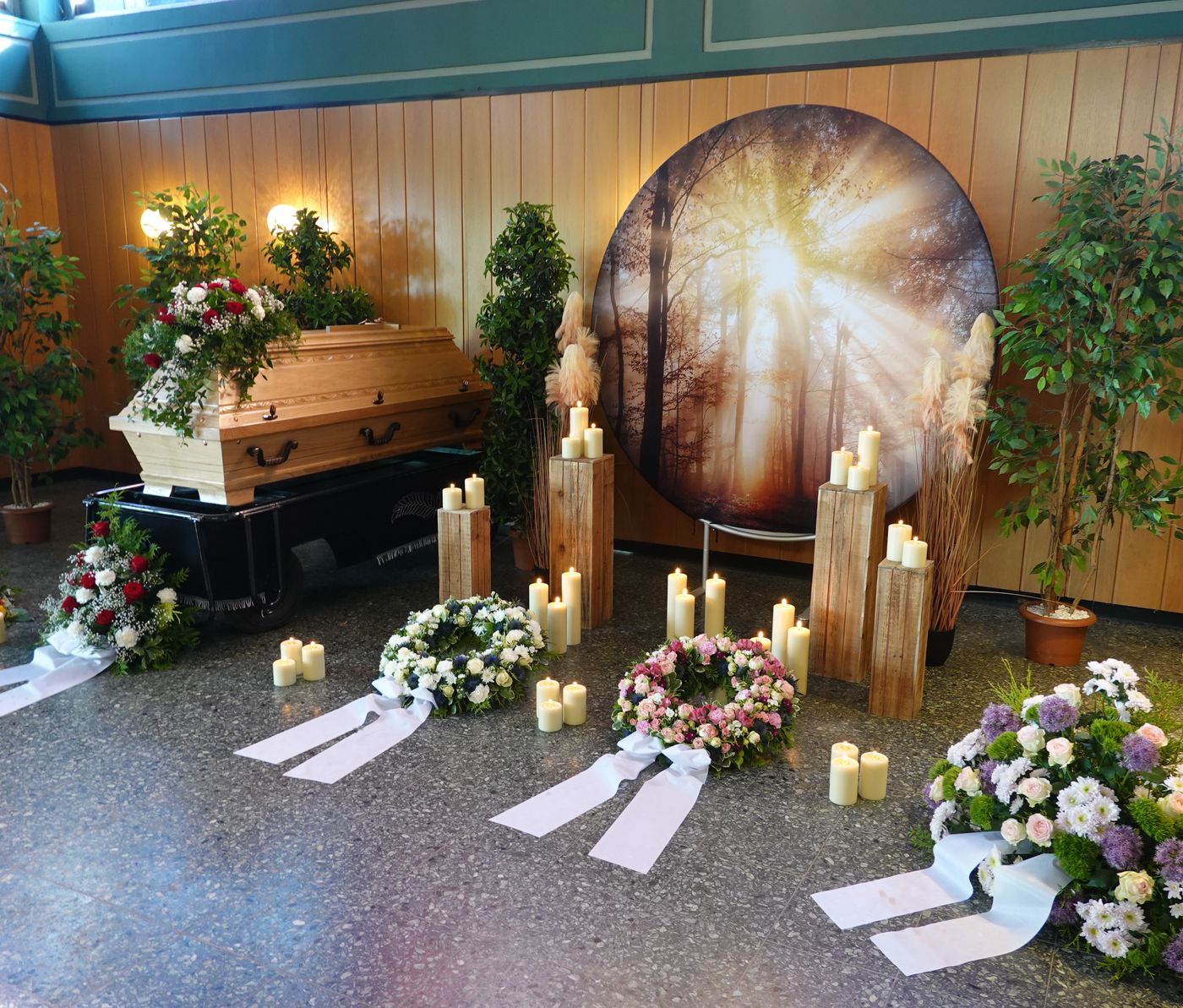 Holzsarg mit Gestecken, Kränzen und Kerzen vor einem Lichtmotiv